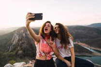 Deux jeunes filles posant pour selfie sur fond de montagnes au soleil . — Photo de stock