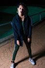 Портрет девушки в городской одежде, позирующей на ночной улице и смотрящей в камеру — стоковое фото