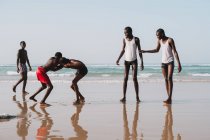 Yoff, Senegal- December 6, 2017: Group of young African men having fun on ocean beach and wrestling cheerfully. — Stock Photo