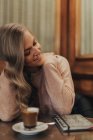 Blonde fille posant au restaurant à côté de la table avec tasse à café et carnet de notes — Photo de stock
