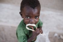 Goree, Senegal- December 6, 2017: Portrait of little black boy biting plastic ribbon at street scene and looking at camera — Stock Photo