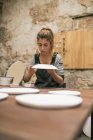 Potter feminino concentrado em avental sentado à mesa e criando placas de barro branco . — Fotografia de Stock