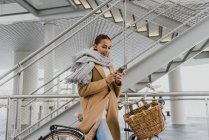Seitenansicht einer Frau mit Fahrrad, die auf dem Parkplatz mit dem Smartphone chattet — Stockfoto