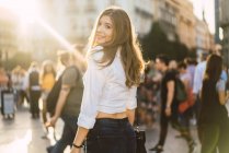 Bruna ragazza in abiti casual guardando oltre la spalla alla fotocamera in piazza della città — Foto stock