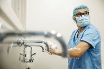 Cirurgião olhando por cima do ombro enquanto lava as mãos antes da operação — Fotografia de Stock