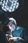 Высокий угол обзора хирургов, оперирующих пациента при свете лампы в больнице — стоковое фото