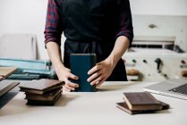 Mid section of man in apron arranging and creating leather notebooks. — Stock Photo