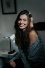 Ritratto di giovane ragazza bruna seduta sul letto e sorridente alla macchina fotografica — Foto stock