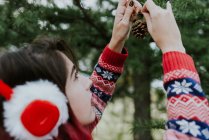 Sobre a visão do ombro da menina na pele orelhas de Natal decorando conífera com cones — Fotografia de Stock