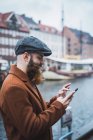 Vista laterale dell'uomo barbuto che naviga smartphone al fiume in città — Foto stock