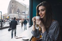 Портрет усміхненої дівчини, що п'є каву в міському кафе — стокове фото