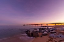 Мальовничий фіолетовий захід сонця на морському березі з довгим пірсом — стокове фото