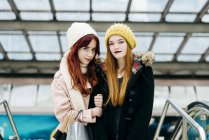 Portrait of young women embracing in mall and looking at camera — Stock Photo