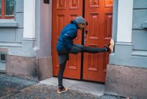 Seitenansicht eines Joggers, der sich mit dem Bein an die Wand lehnt und Muskeln aufwärmt und dehnt — Stockfoto