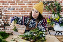 Portrait of woman making Christmas wreath at table against brick wall — Stock Photo