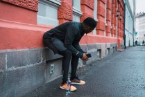 Rückansicht eines Joggers, der sich an die Wand lehnt und sich beugt, um sich mit dem Smartphone in der Hand auszuruhen — Stockfoto