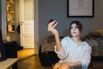 Portrait de femme portant une chemise assise sur le sol à la maison et prenant selfie — Photo de stock
