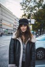 Frau mit stylischer Mütze posiert auf der Straße und blickt in die Kamera — Stockfoto