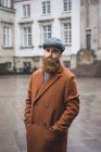 Portrait of bearded man posing in vintage coat and cap posing in city — Stock Photo