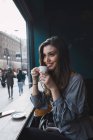 Портрет усміхненої брюнетки п'є каву в кафе і дивиться вбік — стокове фото