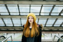 Young pretty woman in yellow knitted hat standing in mall and looking at camera — Stock Photo