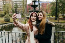 Дві молоді красиві жінки друзі стоять біля фонтану в парку і приймають селфі . — стокове фото