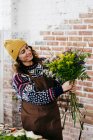 Portrait de fleuriste en pull tricoté et chapeau regardant bouquet dans les mains — Photo de stock