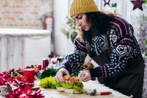 Side view of woman in sweater and hat making floral composition on table — Stock Photo