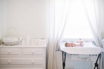 Infant child lying in bed in by window at home. — Stock Photo