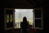 Back view of woman leaning on window sill and looking at nature outside. — Stock Photo