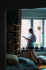 Вид збоку жінки в сорочці читання книги вікном вдома — стокове фото