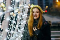 Усміхнена жінка весело позує на святковому освітленні — стокове фото