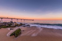 Pôr-do-sol idílico cena na praia com cais e ondas de surf — Fotografia de Stock