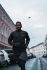 Frontansicht eines athletischen Mannes in warmer Sportbekleidung, der auf der Straße läuft — Stockfoto