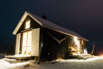 Exterior view of illuminated wooden building in winter forest — Stock Photo