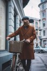 Vue de face de l'homme wering chapeau et manteau marche avec vélo vintage sur la scène de rue — Photo de stock