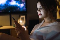 Seitenansicht einer Frau, die abends zu Hause auf dem Smartphone surft — Stockfoto