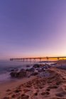 Idyllic sunset scene on beach with pier against sky — Stock Photo