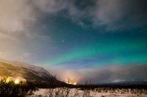 Scenic view of small village in winter meadow over northern lights in sky on background — Stock Photo