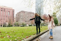 Seitenansicht des Mädchens hilft Freundin beim Balancieren beim Gehen am Rand — Stockfoto