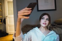 Retrato de mulher tomando selfie com smartphone no chão em casa — Fotografia de Stock