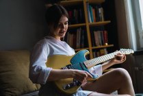 Портрет молодой женщины, позирующей с гитарой на кровати — стоковое фото