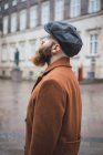 Vista lateral do homem barbudo em posar em casaco e boné e olhando para cima — Fotografia de Stock