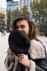 Портрет брюнетки, що ховає посмішку з шапочкою на вулиці — стокове фото
