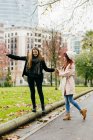 Side view of girl helping girlfriend balancing while walking on edging at park alley — Stock Photo