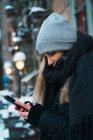 Side view of young blondeoman using smartphone on winter street — Stock Photo