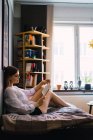 Seitenansicht einer Frau, die zu Hause auf dem Bett sitzt und Buch liest — Stockfoto