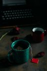 Close-up vista de ups de café e chá à mesa com rosa seca e máquina de escrever retro — Fotografia de Stock