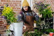 Portrait of woman in hat and apron composing floral composition at floral atelier — Stock Photo