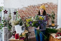 Porträt einer lächelnden Frau im Strickpullover mit Blumenstrauß und Blick in die Kamera — Stockfoto